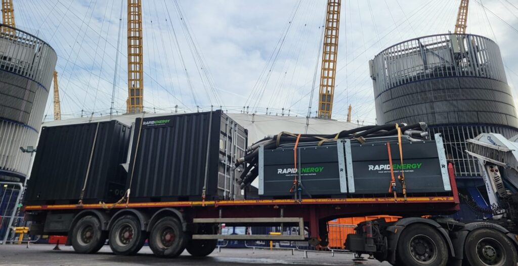 A large transport truck carrying Rapid Energy-branded packaged temporary boilers, parked in front of The O2 Arena.