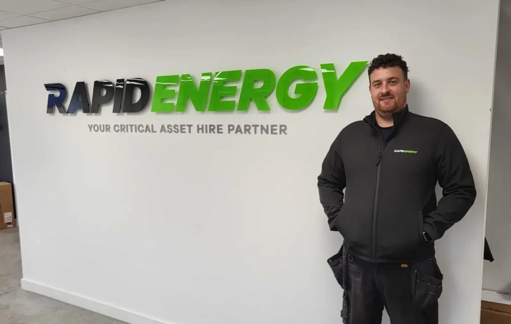 New Rapid Energy employee, Jake Bonser, standing in front of Rapid Energy logo.
