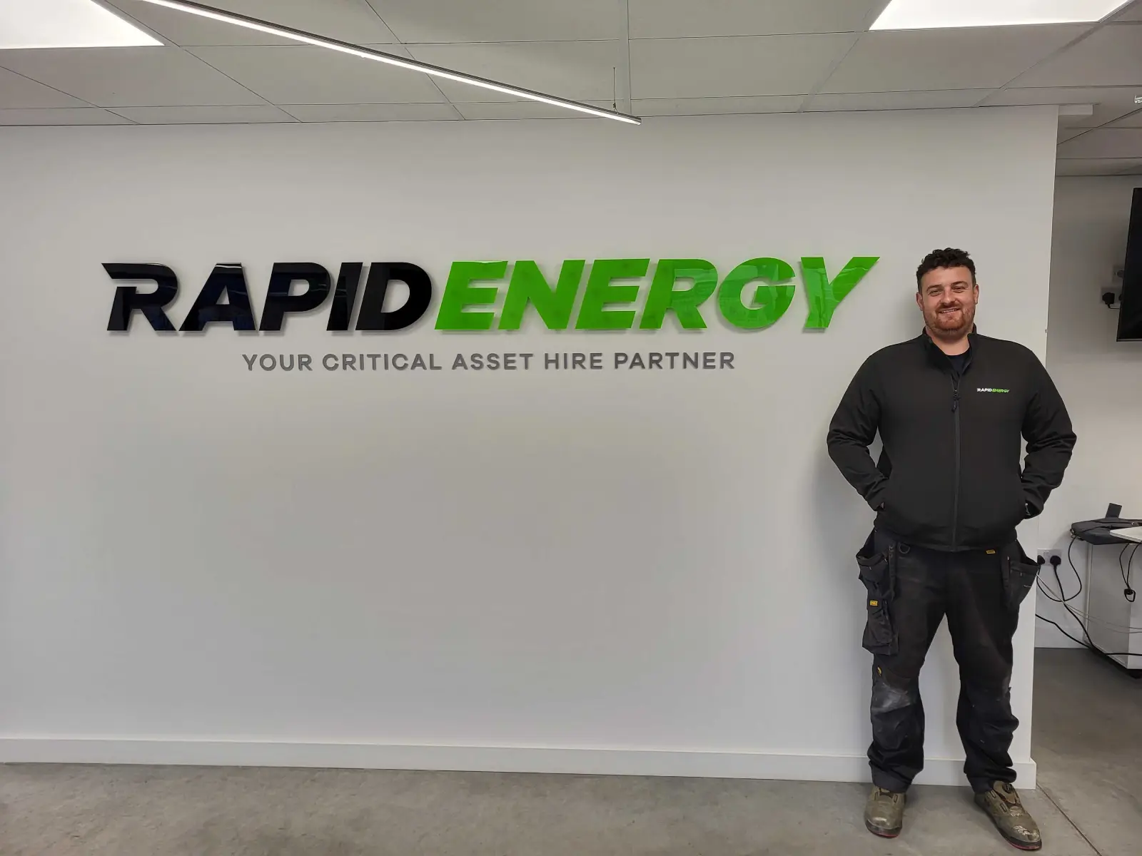 New Rapid Energy employee, Jake Bonser, standing in front of Rapid Energy logo.