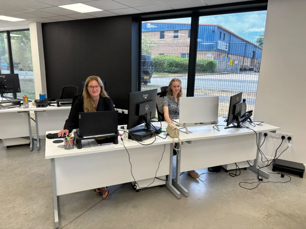 Shanna and Ruby are sitting at their laptops in the Rapid Energy Redditch depot.