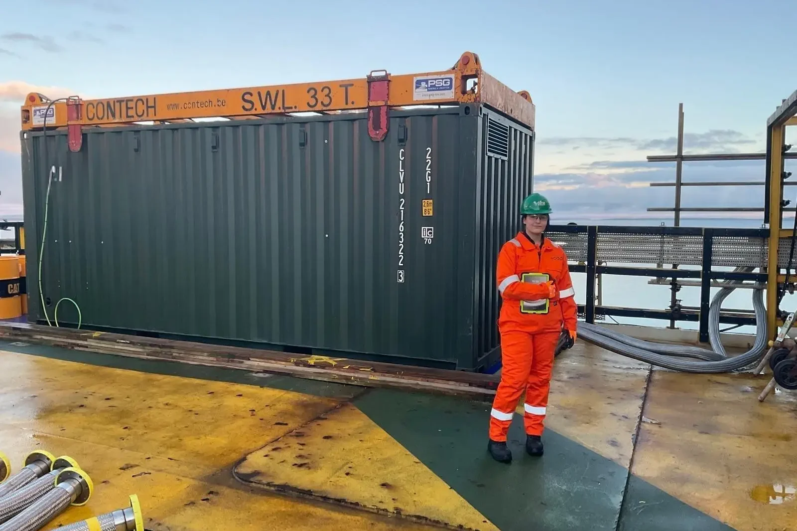 Victoria Hooper, a junior engineer at Rapid Energy, working on-site to install and test a temporary boiler system. She is wearing high-visibility PPE, including an orange coverall, gloves, and a green hard hat branded with Dana Petroleum.