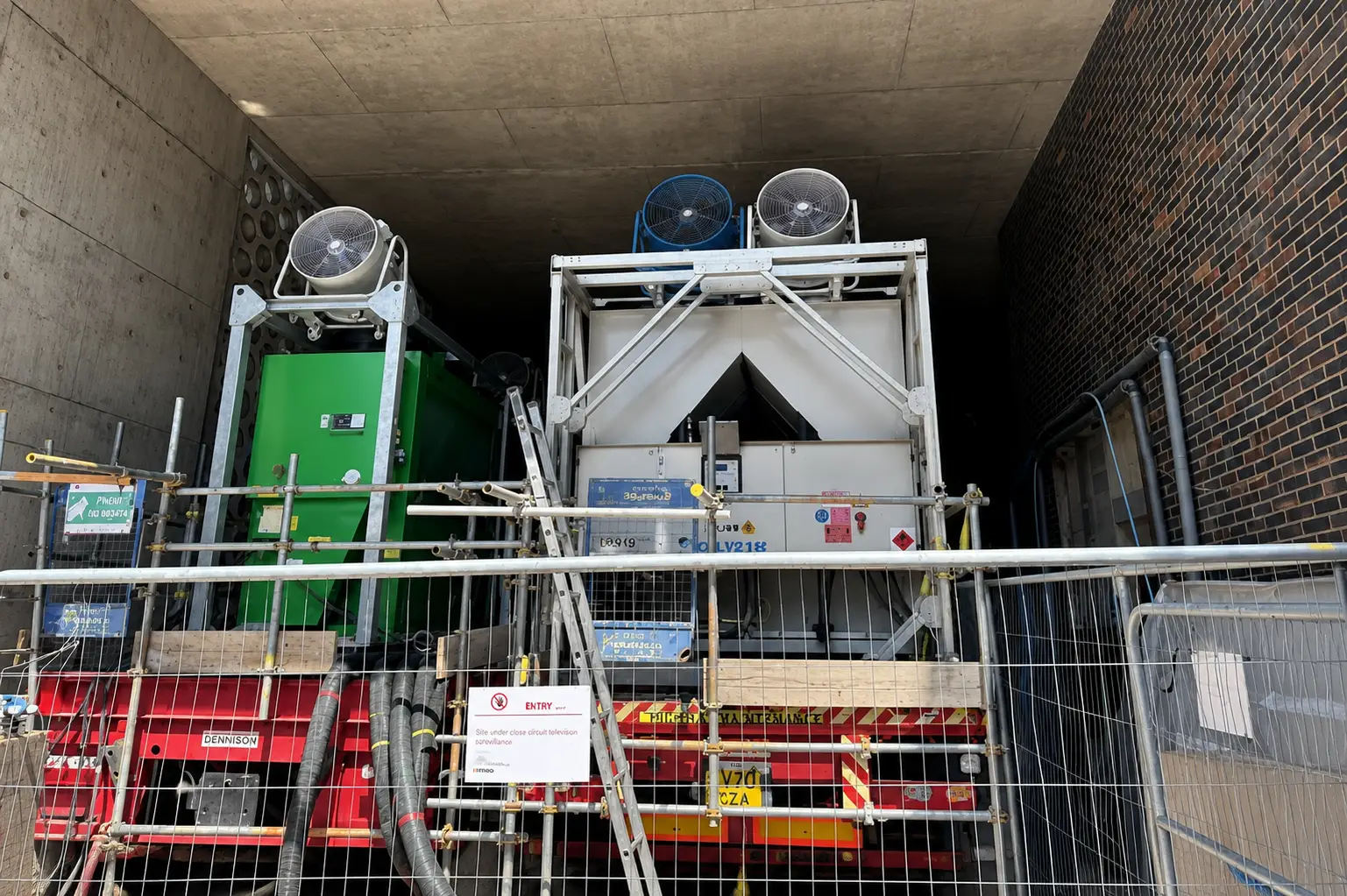 Trailer-mounted air-cooled chillers installed within the confined tunnel-like space, with high-level extraction fans removing condenser discharge air exceeding 90°C.